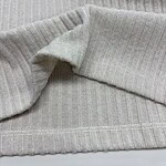 Close-up of light gray ribbed knit fabric, showcasing its texture and fine vertical lines, ideal for sweaters and casual wear.