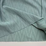 Close-up of mint green fabric with a textured, wavy pattern, showcasing its soft and luxurious appearance, ideal for fashion and interior design.