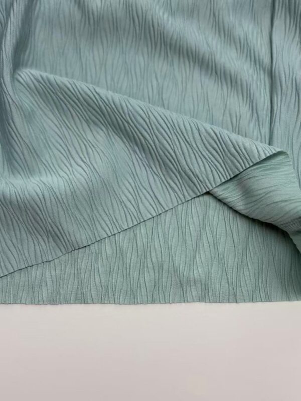 Close-up of mint green fabric with a textured, wavy pattern, showcasing its soft and luxurious appearance, ideal for fashion and interior design.