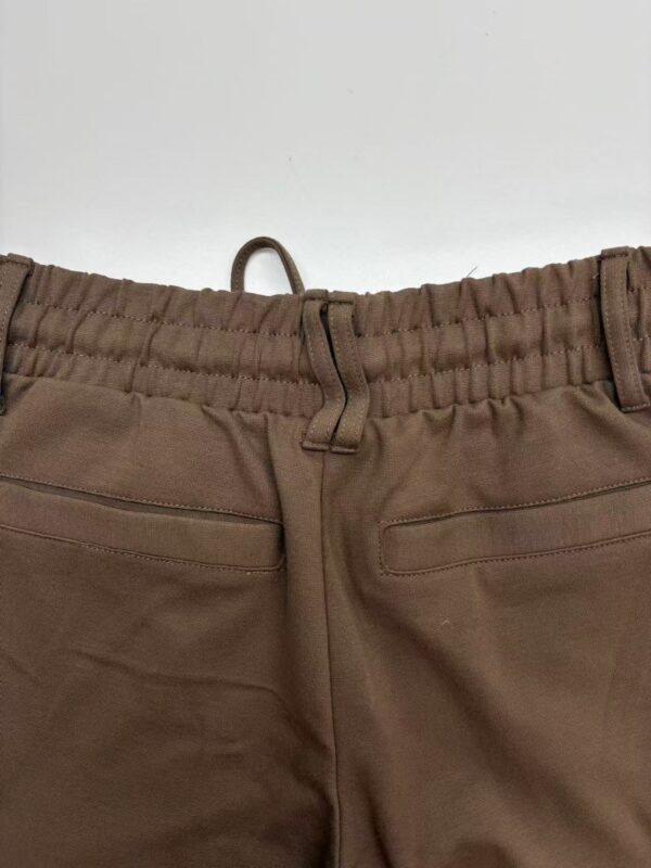 Close-up of brown casual pants featuring an elastic waistband, belt loops, and two front pockets, suitable for everyday wear.