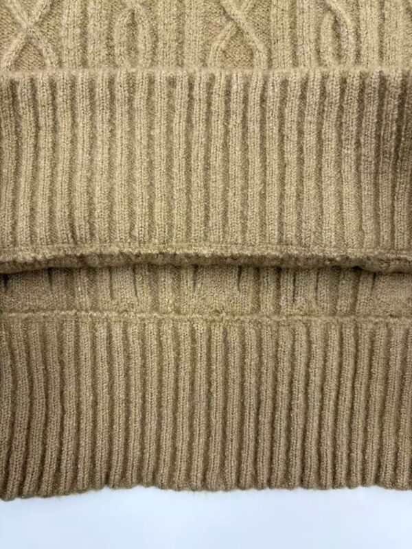 Close-up of a beige cable knit sweater with ribbed cuffs and intricate cable patterns, showcasing high-quality knitwear suitable for cold weather.