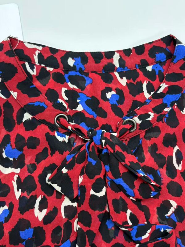 Close-up of a stylish animal print blouse with a bow tie detail, featuring red, black, white, and blue colors, perfect for fashion-forward outfits.