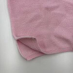 Close-up of a pink knitted sweater fabric showing fine texture and stitching details.