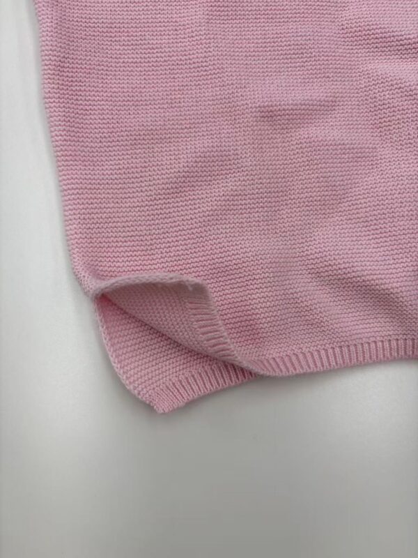 Close-up of a pink knitted sweater fabric showing fine texture and stitching details.