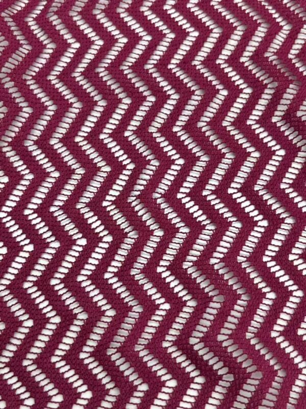 Close-up of burgundy fabric with white zigzag pattern, showcasing intricate textile design suitable for fashion and home decor.