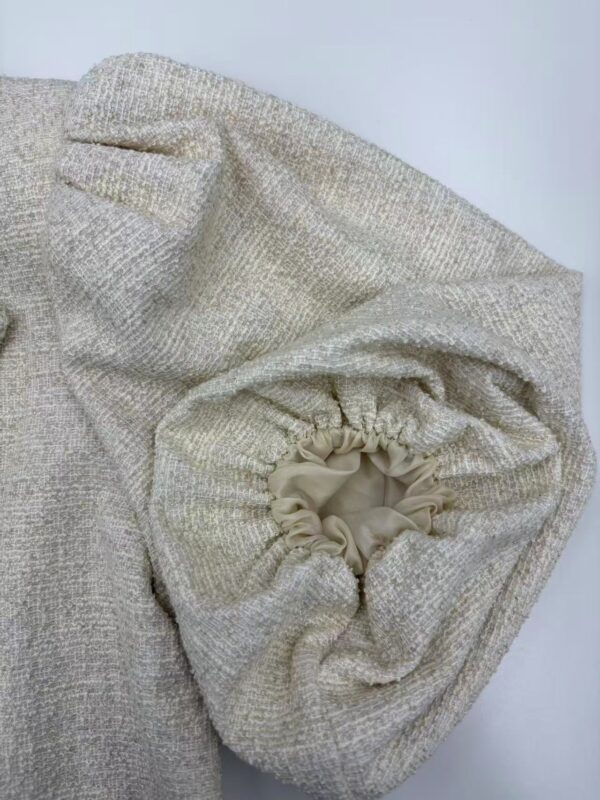 Close-up of a beige knitted sweater with a drawstring detail, showcasing soft textured fabric and stylish design for casual or chic wear.