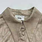 Close-up of a beige satin blouse with a pointed collar and button details, perfect for stylish women's fashion.