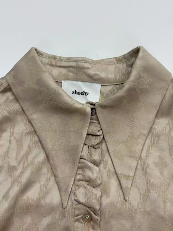 Close-up of a beige satin blouse with a pointed collar and button details, perfect for stylish women's fashion.