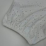 Close-up of white eyelet fabric with embroidered holes and elastic edge, suitable for clothing or home textiles.