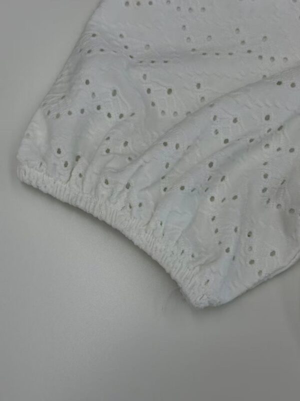 Close-up of white eyelet fabric with embroidered holes and elastic edge, suitable for clothing or home textiles.