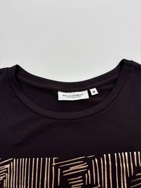 Close-up of a black T-shirt featuring a gold geometric pattern on the front, with a round neckline and a size M label from Broadway.