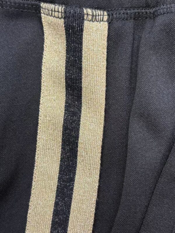 Close-up of black pants featuring beige and black vertical stripe detail, showcasing stylish and modern design elements.