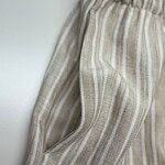 Close-up of beige linen pants with white vertical stripes, elastic waistband, and side pocket, perfect for casual summer wear.