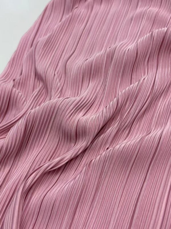 Close-up of pink pleated fabric with fine vertical lines, showcasing texture and flow, ideal for stylish clothing and fashion design.