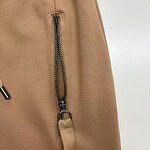 Close-up of beige pants featuring a prominent zipper and strap detail, showcasing stylish casual wear for women.
