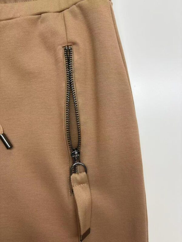 Close-up of beige pants featuring a prominent zipper and strap detail, showcasing stylish casual wear for women.
