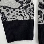 Close-up of a black and white knitted sweater featuring reindeer and snowflake patterns, with a black ribbed cuff.