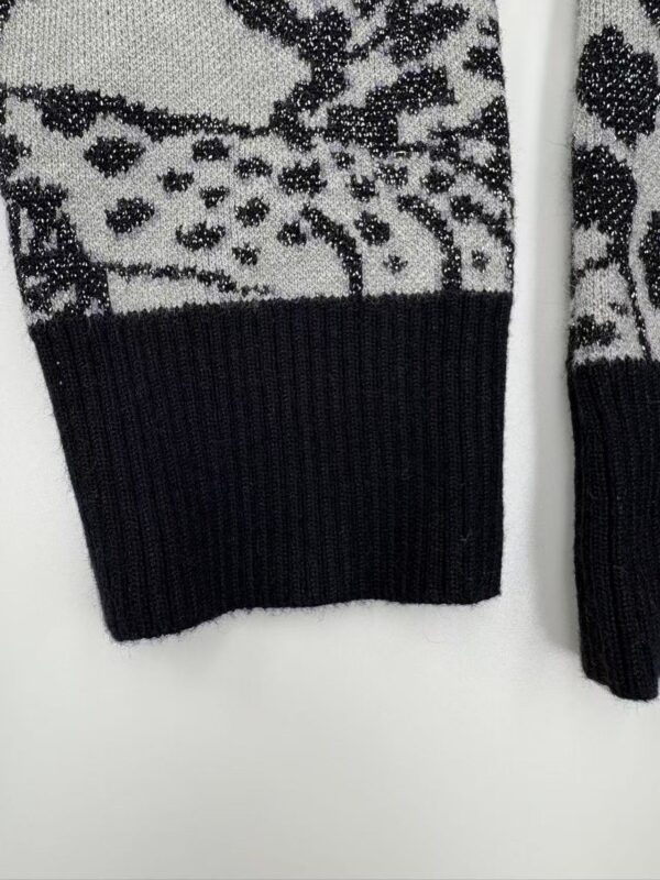 Close-up of a black and white knitted sweater featuring reindeer and snowflake patterns, with a black ribbed cuff.