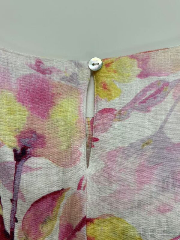 Close-up of floral fabric with a small white button at the top, showcasing a delicate, colorful floral pattern in pink, yellow, and purple hues.