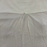 Close-up of beige dress fabric with pleats and a small decorative button at the waist, showcasing high-quality material and craftsmanship.