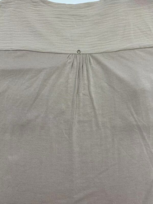 Close-up of beige dress fabric with pleats and a small decorative button at the waist, showcasing high-quality material and craftsmanship.