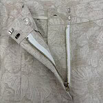 Close-up of light beige linen pants featuring a front zipper and button closure, showcasing a casual and breathable fabric suitable for warm weather.