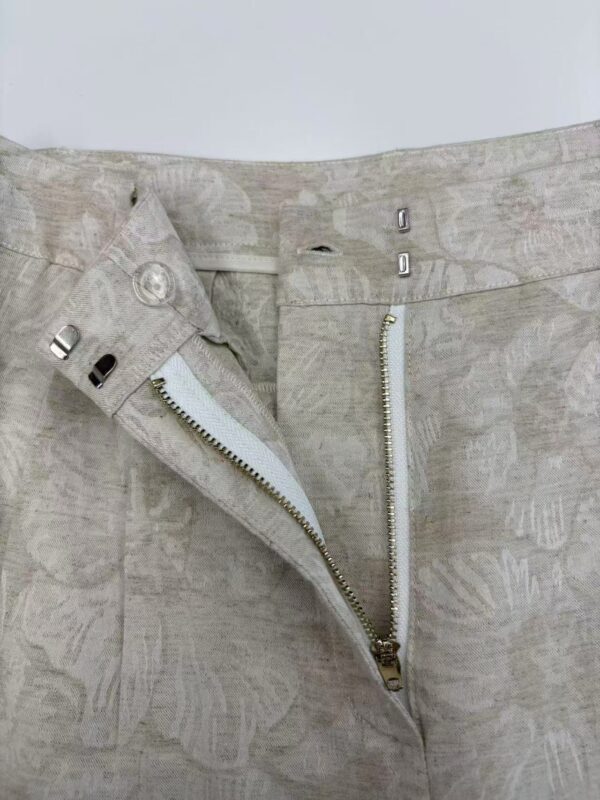 Close-up of light beige linen pants featuring a front zipper and button closure, showcasing a casual and breathable fabric suitable for warm weather.