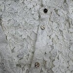 Close-up of a white lace dress with decorative buttons, showcasing intricate lace patterns and fine craftsmanship.