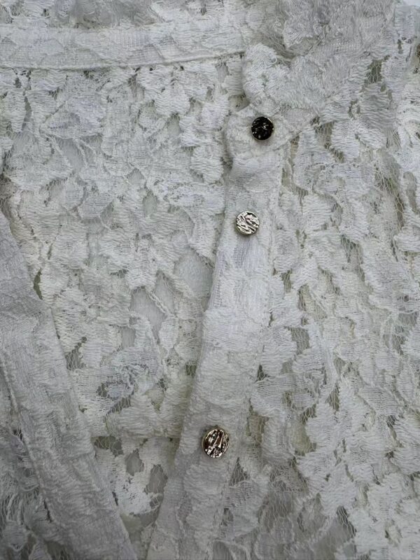 Close-up of a white lace dress with decorative buttons, showcasing intricate lace patterns and fine craftsmanship.