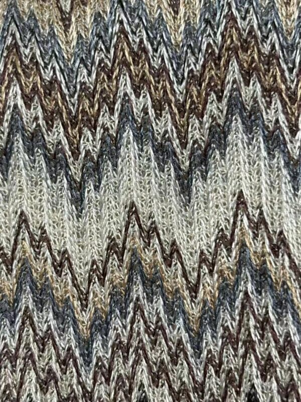 Close-up of a textured fabric featuring a zigzag pattern in shades of brown, beige, black, and white, showcasing intricate weaving details.