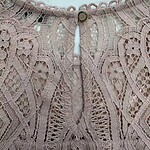Close-up of intricate pink lace fabric with detailed embroidery and scalloped edges, showcasing craftsmanship and delicate design.