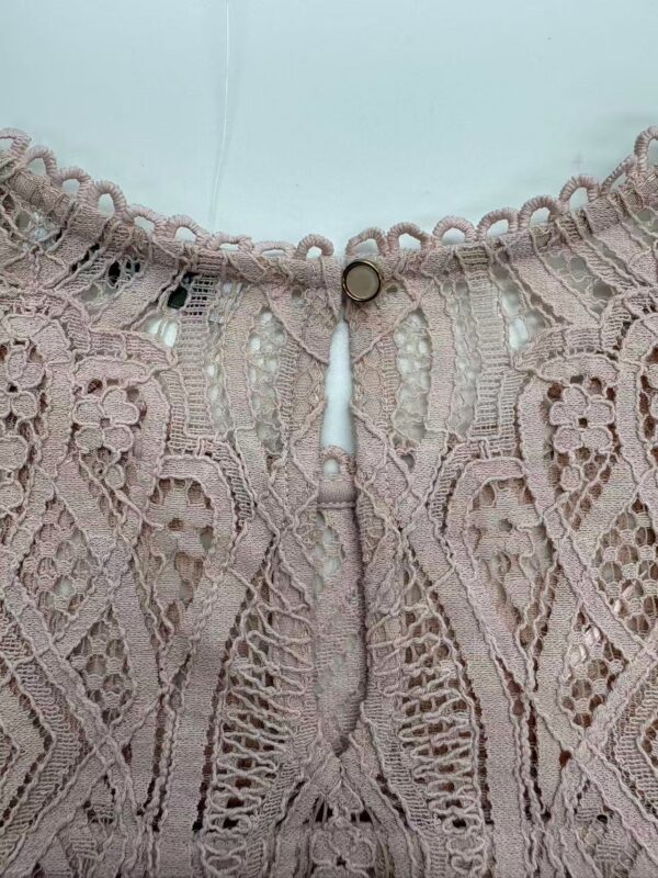 Close-up of intricate pink lace fabric with detailed embroidery and scalloped edges, showcasing craftsmanship and delicate design.