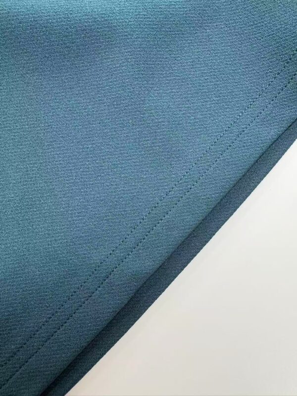 Detailed close-up of blue fabric material with visible stitching, suitable for fashion or textile product descriptions.