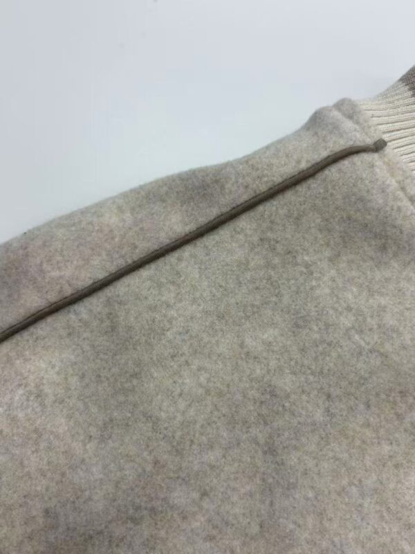 Detailed close-up of a beige woolen sweater showing texture and stitching details.