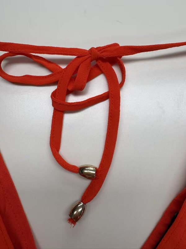 Close-up of a red cord necklace with silver beads, tied in a bow, on a white background, showcasing stylish jewelry design.