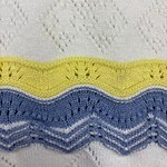 Close-up of a knitted fabric with white, yellow, blue, and gray wavy and diamond patterns, showcasing detailed stitching and texture.