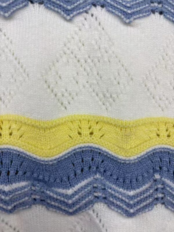 Close-up of a knitted fabric with white, yellow, blue, and gray wavy and diamond patterns, showcasing detailed stitching and texture.