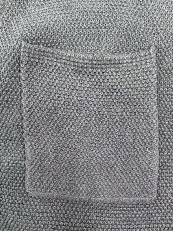 Close-up of a textured fabric pocket on a garment, showcasing detailed stitching and pattern in neutral tones.