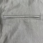 Detailed close-up of light gray fabric with a horizontal zipper, showcasing smooth texture and fine stitching, ideal for fashion or clothing product images.