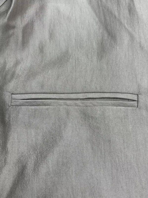 Detailed close-up of light gray fabric with a horizontal zipper, showcasing smooth texture and fine stitching, ideal for fashion or clothing product images.