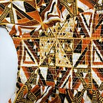 Close-up of vibrant African print fabric featuring geometric shapes in orange, black, white, and yellow, showcasing traditional textile design.