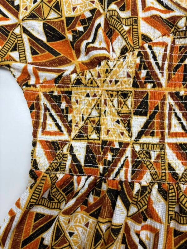 Close-up of vibrant African print fabric featuring geometric shapes in orange, black, white, and yellow, showcasing traditional textile design.