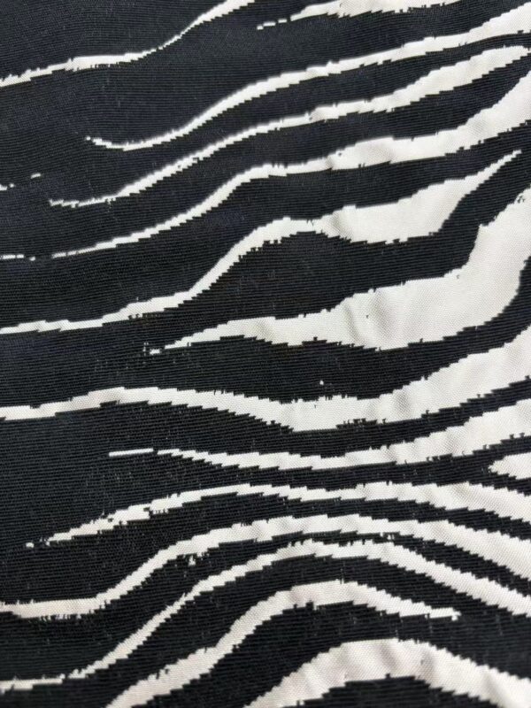 Close-up of black and white zebra print fabric, showcasing wavy stripes and textured material, ideal for stylish clothing and accessories.