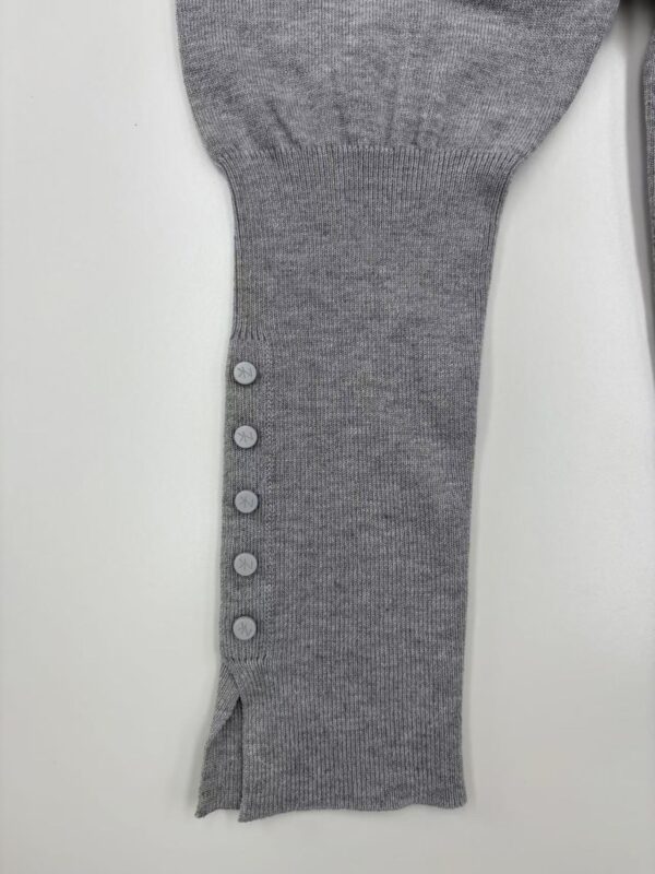 Close-up of a gray knit sweater sleeve featuring a row of five buttons and a small slit at the cuff, showcasing detailed craftsmanship and soft fabric.