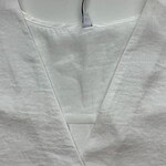 Close-up of a white medical gown with a V-neck design, hanging on a hook, suitable for healthcare professionals and medical settings.