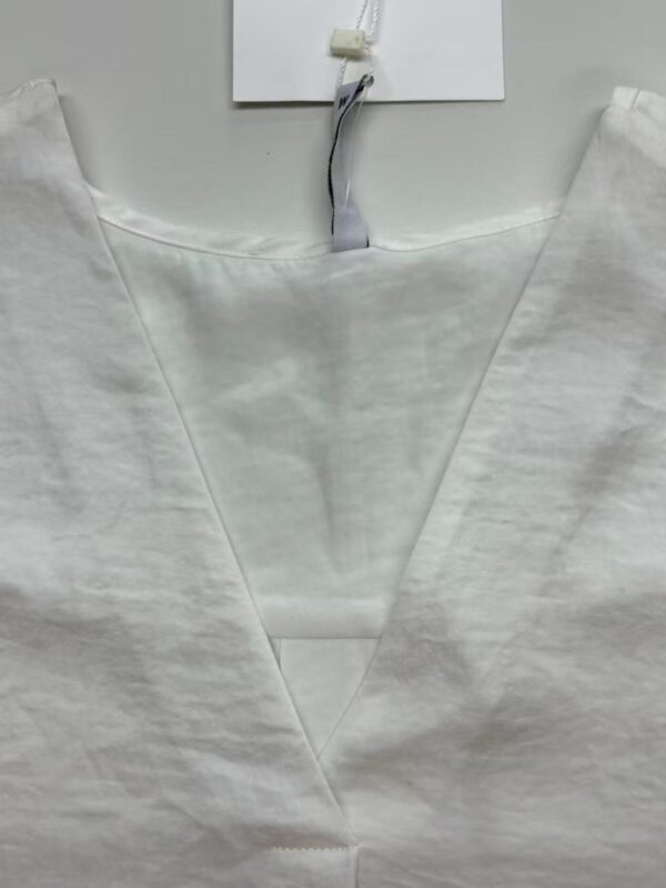 Close-up of a white medical gown with a V-neck design, hanging on a hook, suitable for healthcare professionals and medical settings.