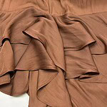 Close-up of luxurious brown satin fabric with flowing, ruffled texture, ideal for high-end fashion design and elegant clothing.