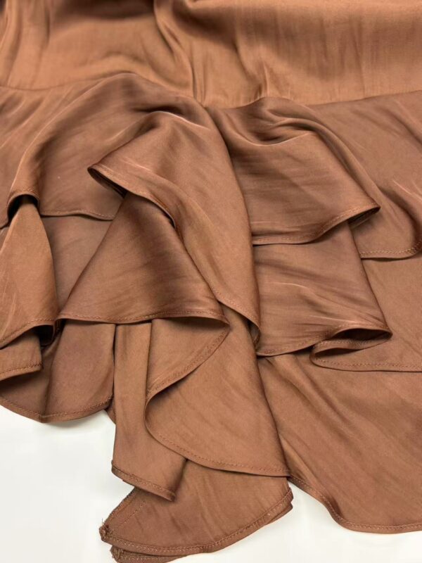 Close-up of luxurious brown satin fabric with flowing, ruffled texture, ideal for high-end fashion design and elegant clothing.