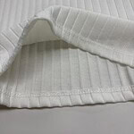 Close-up of white ribbed fabric with a folded edge, showcasing texture and pattern suitable for clothing or textile design.