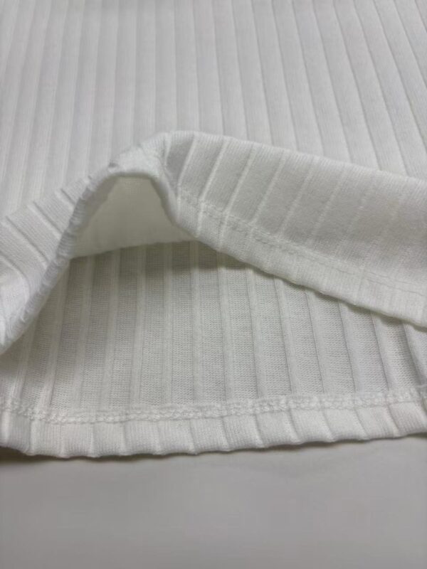 Close-up of white ribbed fabric with a folded edge, showcasing texture and pattern suitable for clothing or textile design.